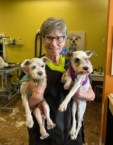 An Uptown team member smiling with two small dogs in the salon